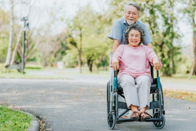 Asian senior woman in a wheelchair walking outside with her husband family caregiver demand is skyrocketing
