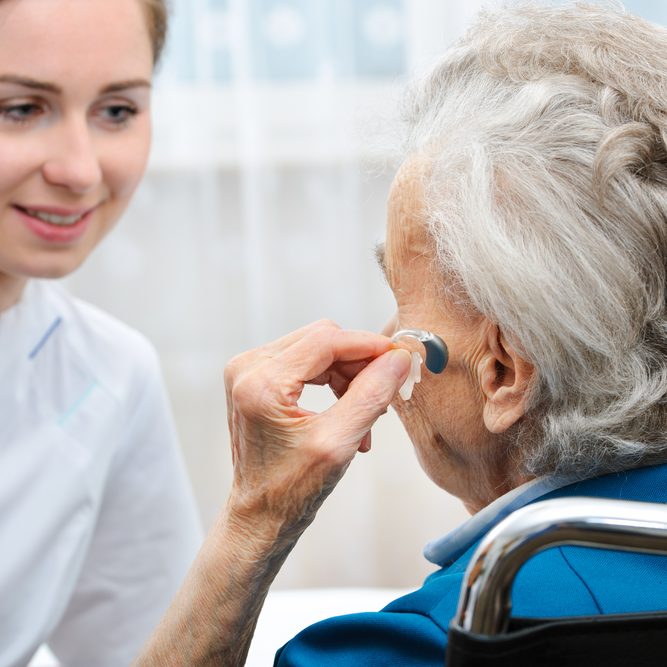 Senior woman with a hearing aid Senior woman inserts hearing aid in her ear learning about Cognitive Decline in Seniors from nurse
