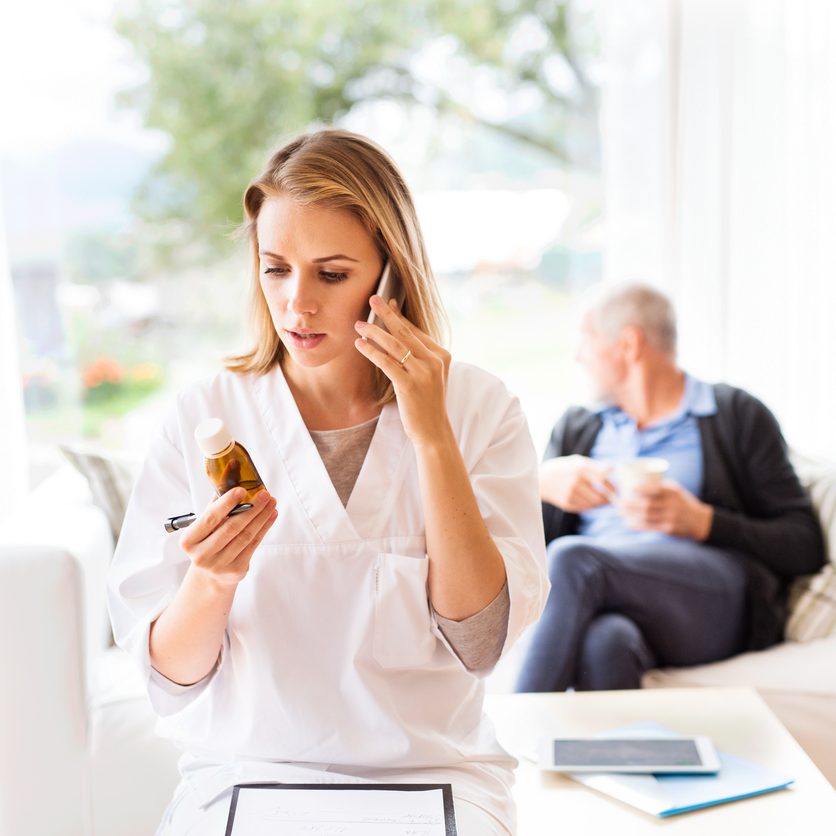 Health visitor with smartphone and a senior man during home visit. A female nurse or a doctor making a phone call. long-distance caregiving concept