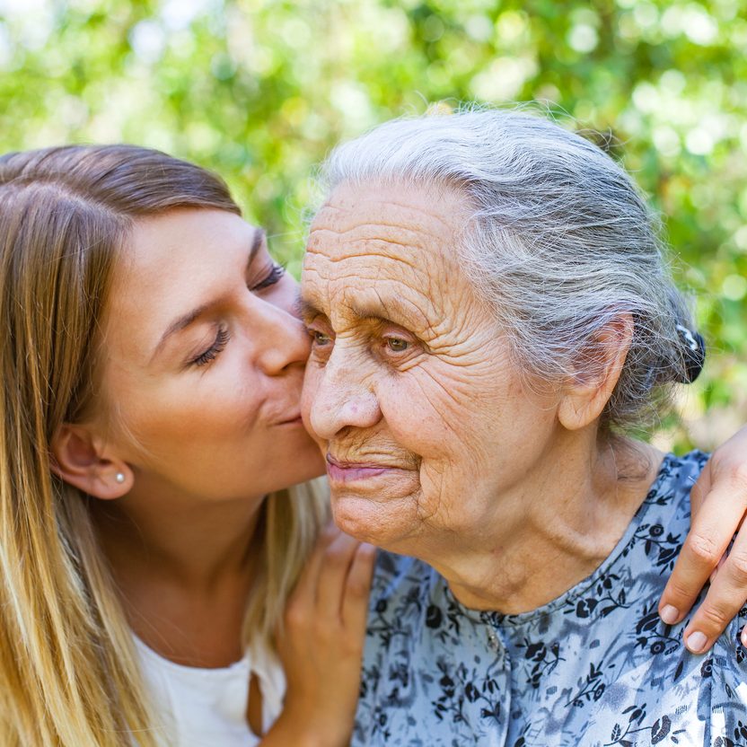 Young woman kissing her old grandmother in the park. Living with dementia concept