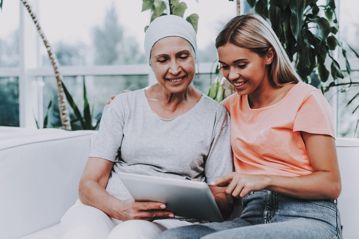 Caregiver helps cancer patient with medication management on her tablet.