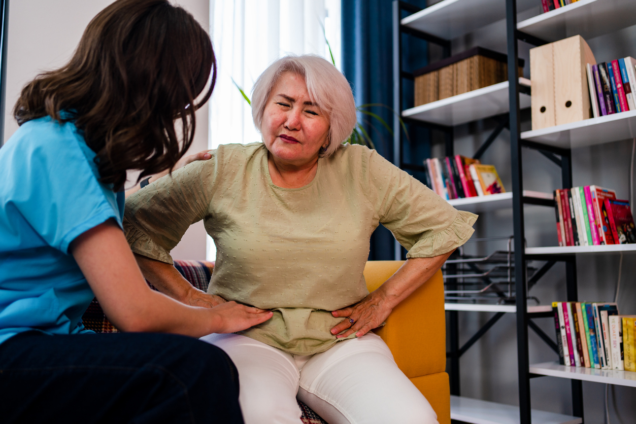 Elderly woman explains GERD pain to caregiver in Nassau County.