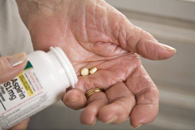 Elderly woman has two aspirin in her hand to take for cardiovascular health.