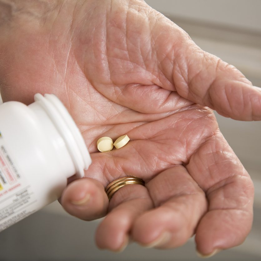 Elderly woman has two aspirin in her hand to take for cardiovascular health.