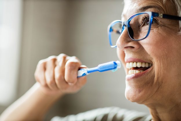 Elderly woman in Staten Island brushes her teeth as part of good oral hygiene.