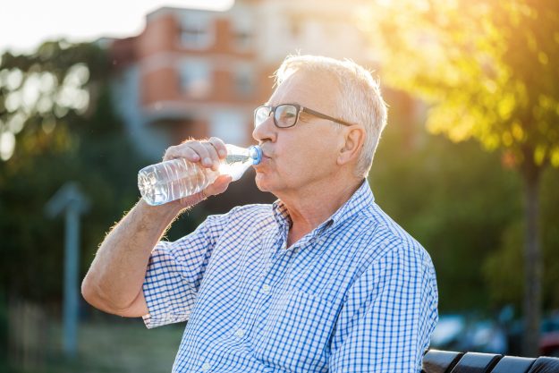 Elderly man with congestive heart failure drinks water outdoors to maintain fluid balance.