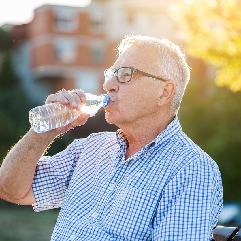 Elderly man with congestive heart failure drinks water outdoors to maintain fluid balance.