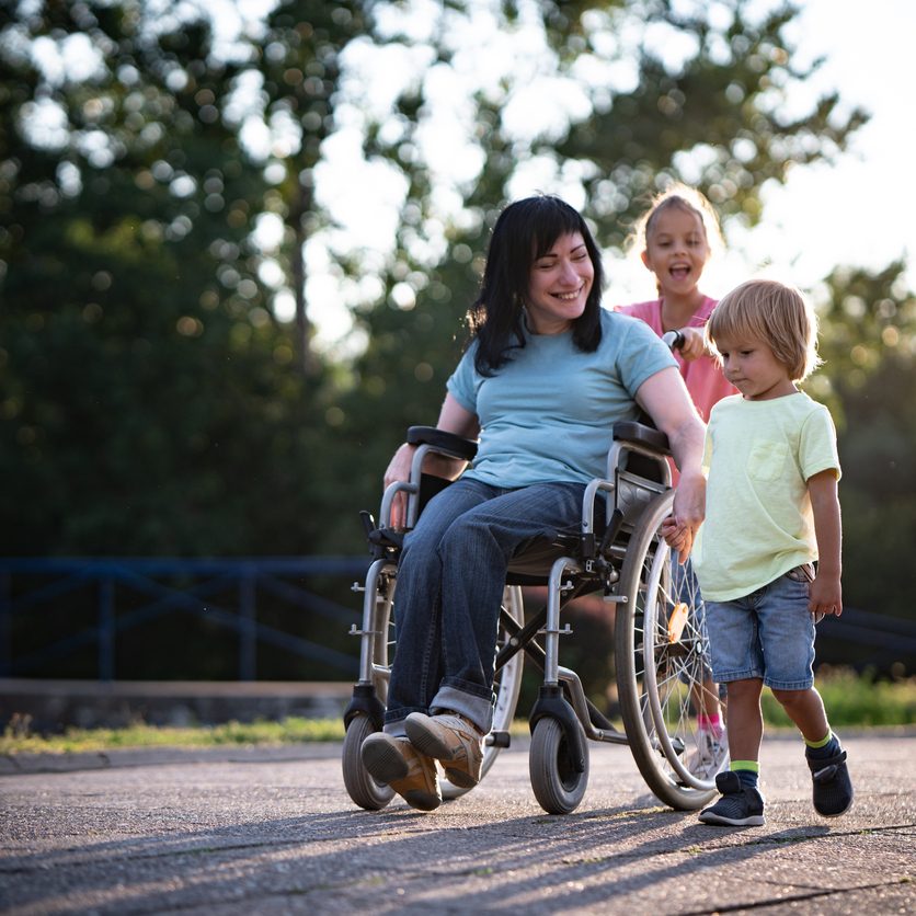 A mother with a spinal cord injury is spending time outside with her children.