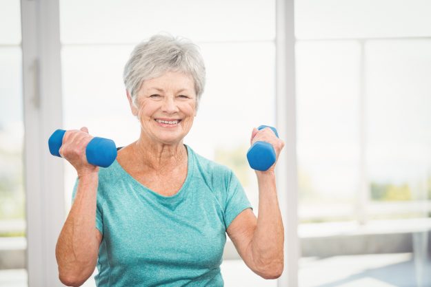 An elderly woman lifts free weights as part of her home exercise plan.