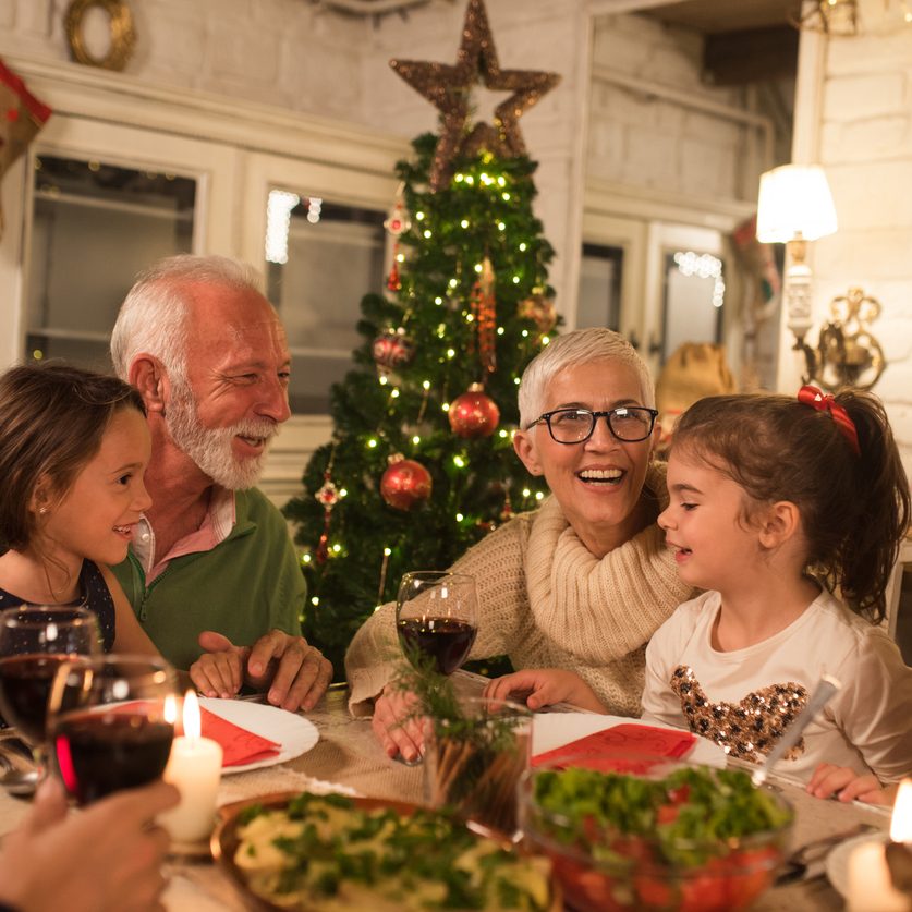 An elderly couple enjoys a holiday dinner with family, after traveling and implementing holiday safety tips.