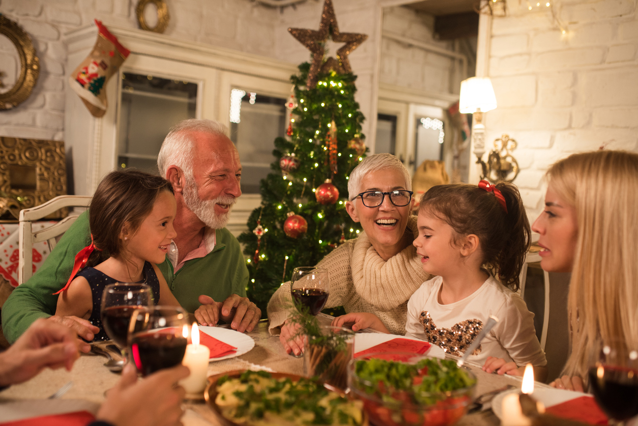 An elderly couple enjoys a holiday dinner with family, after traveling and implementing holiday safety tips.