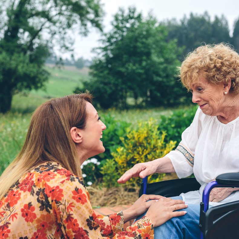 Young woman smiles at woman in wheelchair with Frontotemporal Dementia.