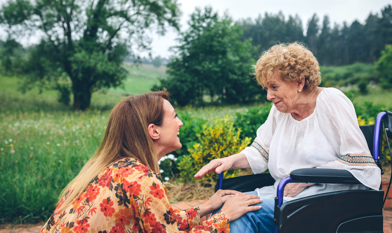 Young woman smiles at woman in wheelchair with Frontotemporal Dementia.